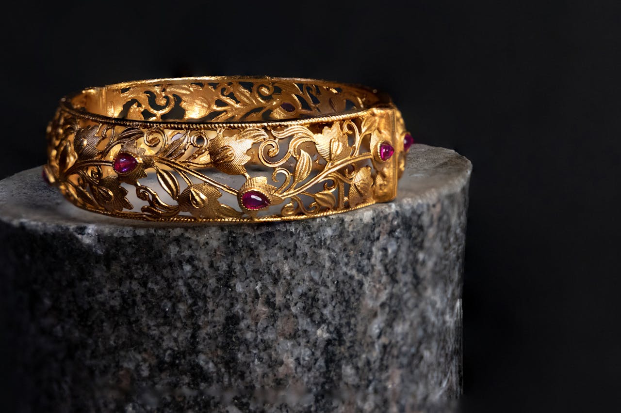 Intricate gold bracelet with ruby accents on a dark background. Luxurious and elegant design.